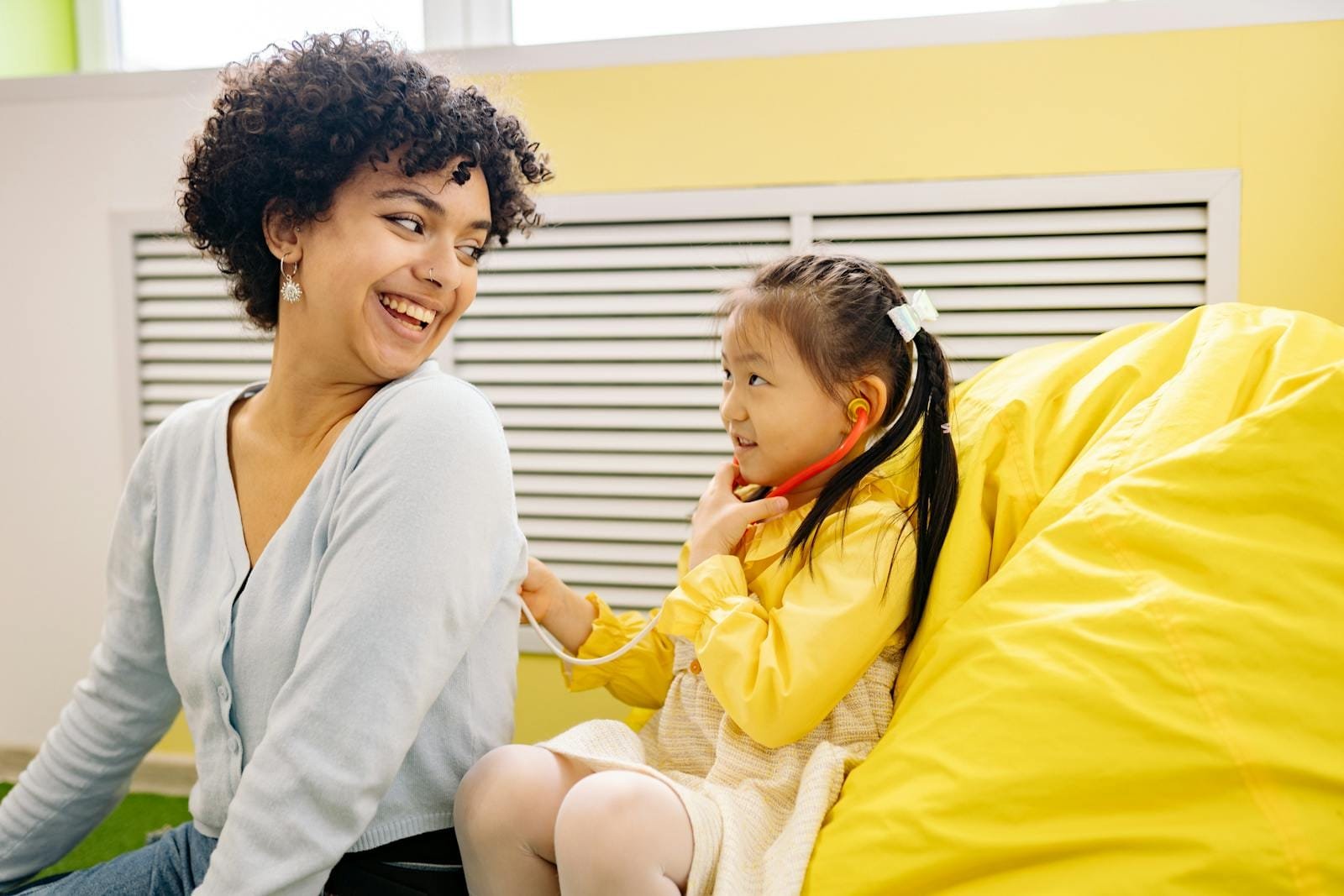 Smiling woman and child playing with stethoscope indoors. Bright, playful and happy moment.